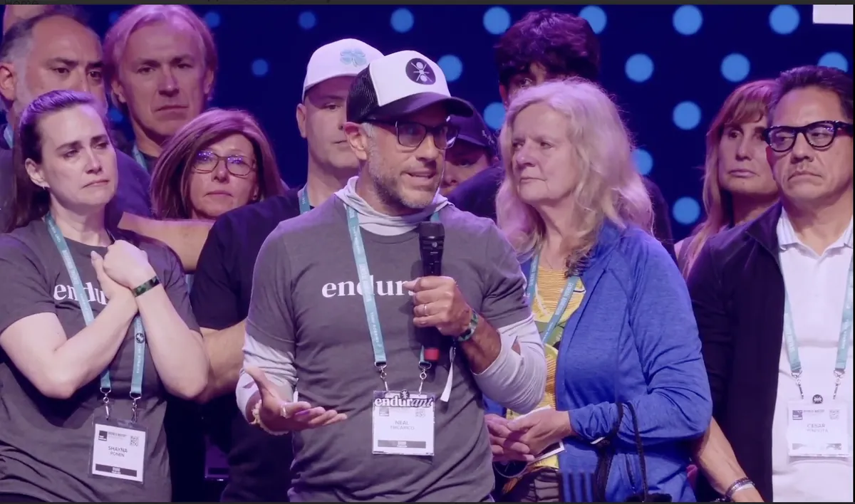 Neal Tricarico speaking on stage, surrounded by the Endurant community